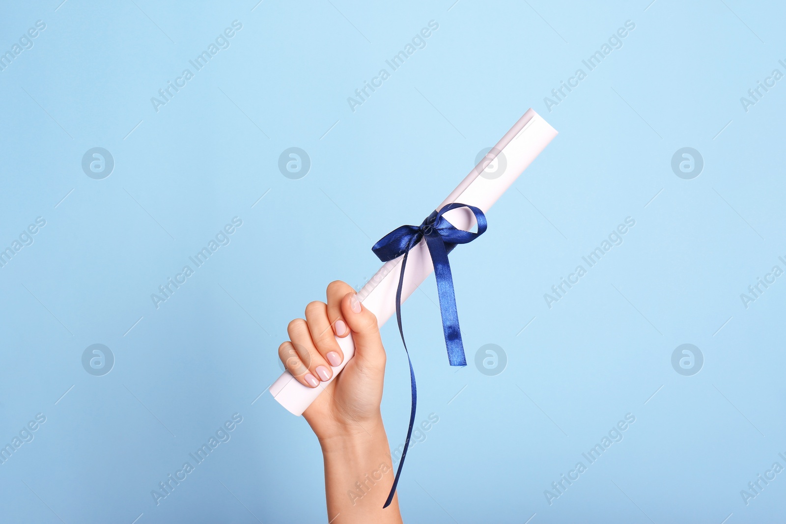 Photo of Student holding rolled diploma with ribbon on light blue background, closeup