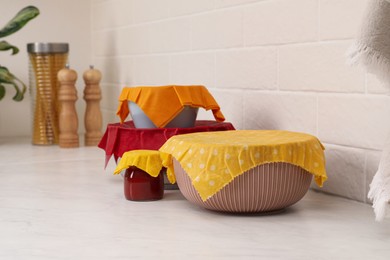 Photo of Different dishware covered with beeswax food wraps on white table. Space for text