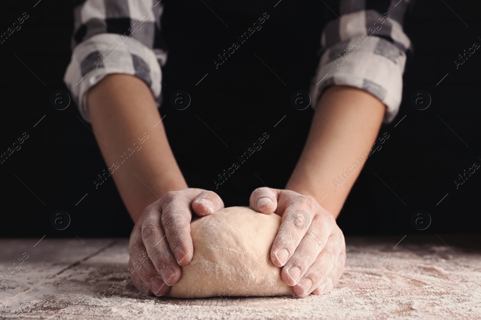 Photo of Man kneading dough at wooden table on dark background, closeup