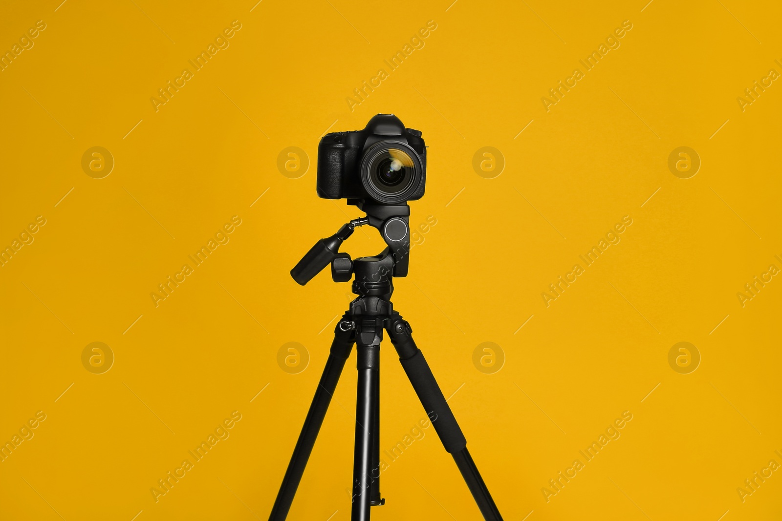 Photo of Modern tripod with professional camera on yellow background