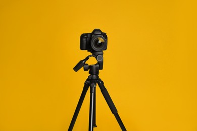 Modern tripod with professional camera on yellow background