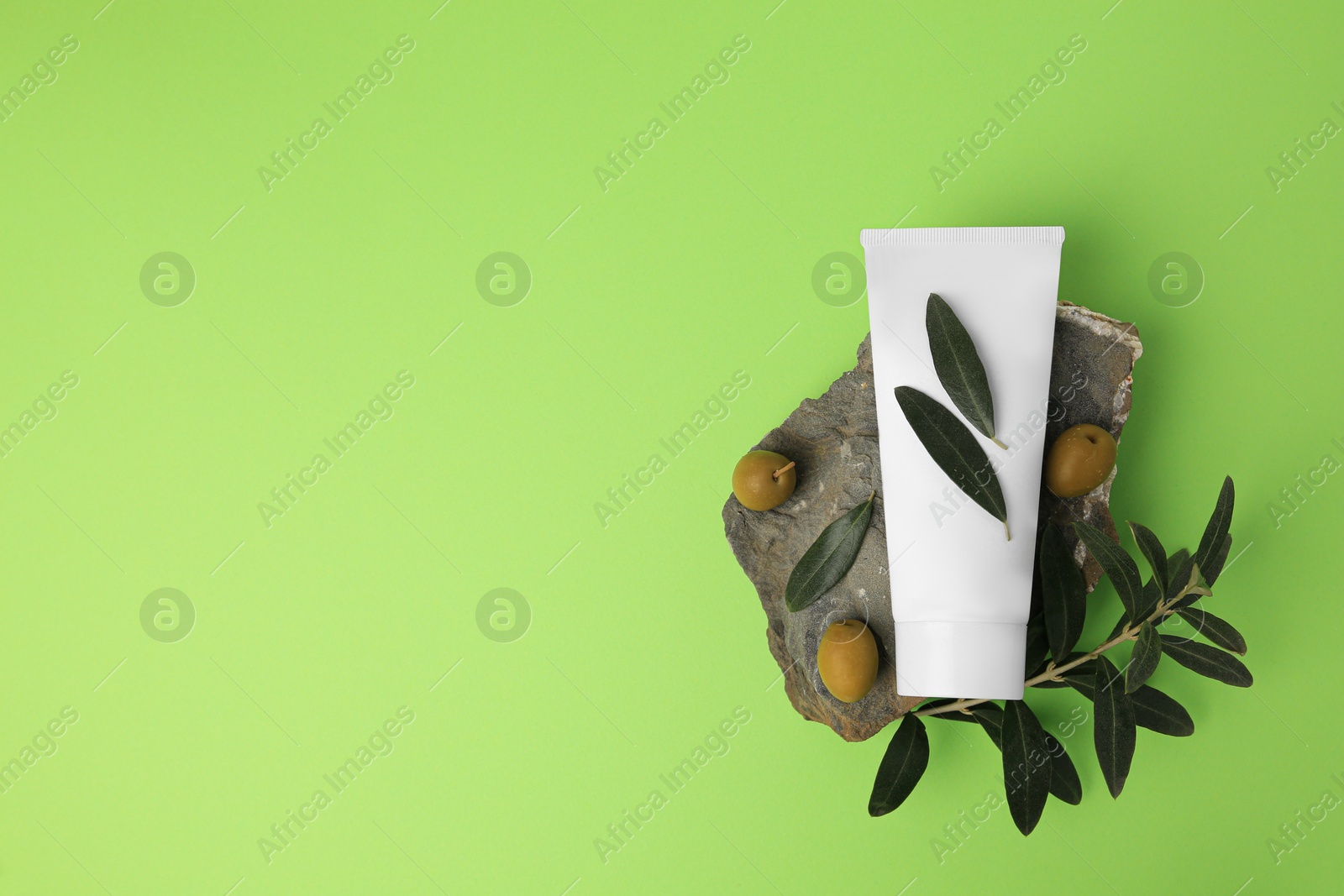 Photo of Tube of cream and olives on light green background, flat lay. Space for text