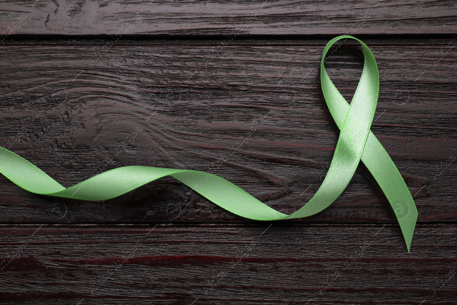 Photo of World Mental Health Day. Green ribbon on wooden background, top view