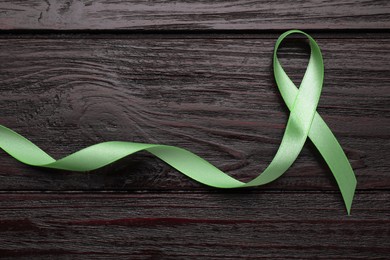 World Mental Health Day. Green ribbon on wooden background, top view