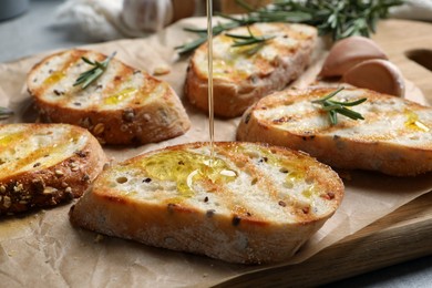 Pouring oil onto slice of toasted bread on wooden board, closeup