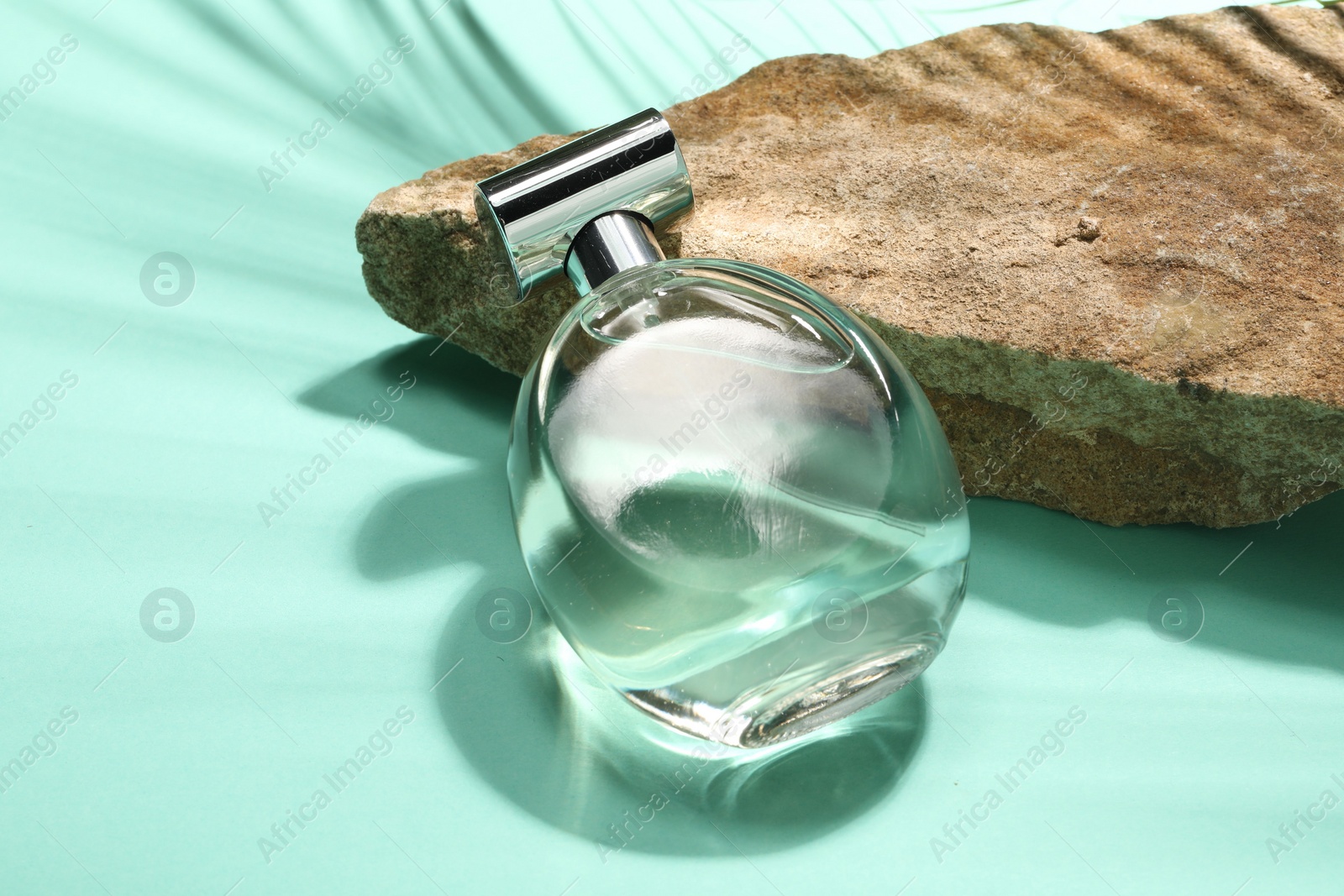 Photo of Bottle of luxury perfume in sunlight and stone on turquoise background