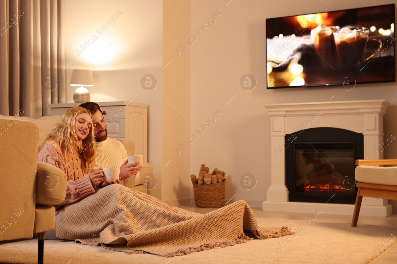 Photo of Lovely couple with hot drinks spending time together near fireplace at home