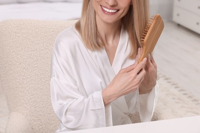 Woman brushing her hair indoors, closeup view