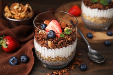 Photo of Tasty granola with berries, yogurt and chia seeds in glass on wooden table, closeup