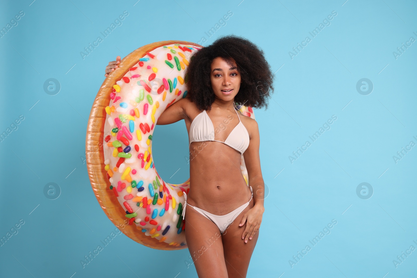Photo of Beautiful woman in stylish bikini with inflatable ring on light blue background