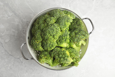 Photo of Fresh green broccoli in colander on grey marble table, top view