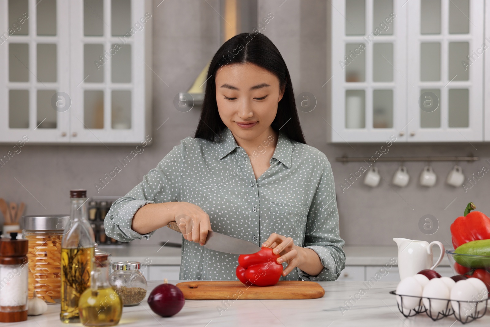 Photo of Cooking process. Beautiful woman cutting bell pepper at white countertop in kitchen