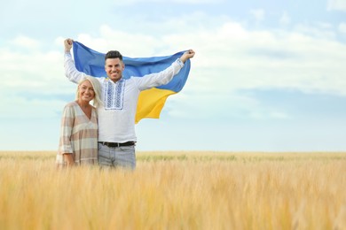 Man with mother holding national flag of Ukraine in field. Space for text