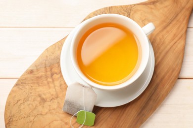 Photo of Tea bag and cup of hot beverage on light wooden table, top view