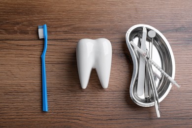 Photo of Tooth shaped holder, brush and tray with dentist's tools on wooden table, flat lay