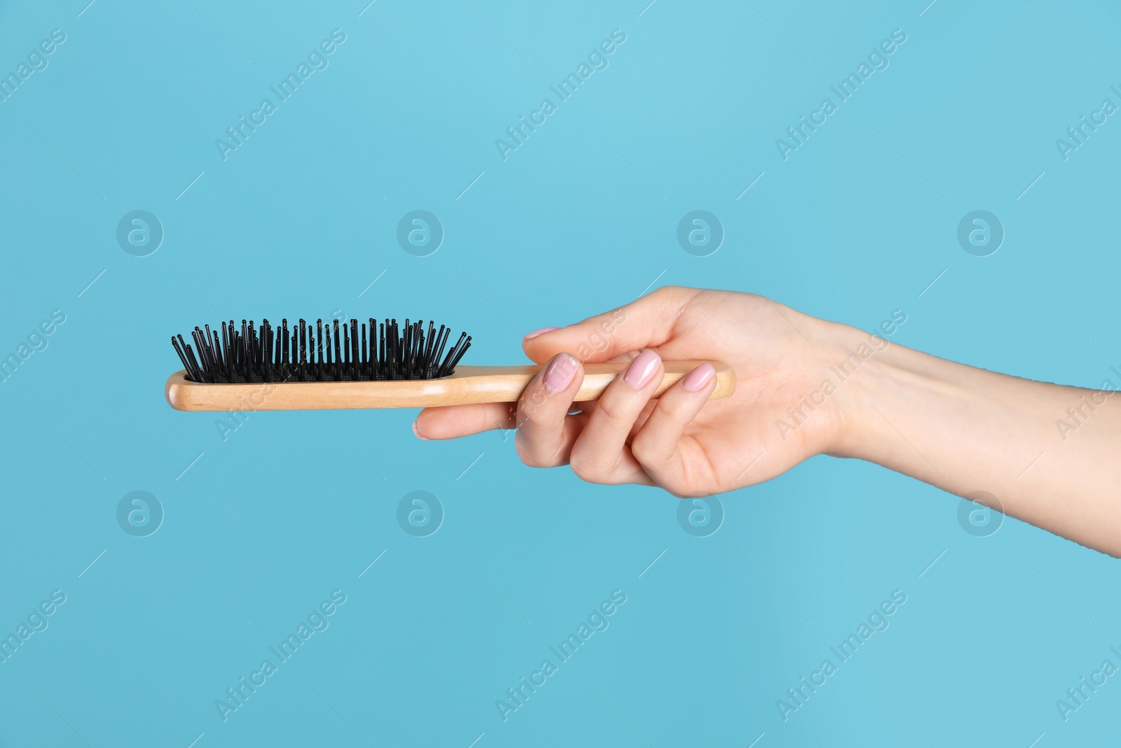 Photo of Woman holding wooden hair brush against blue background, closeup