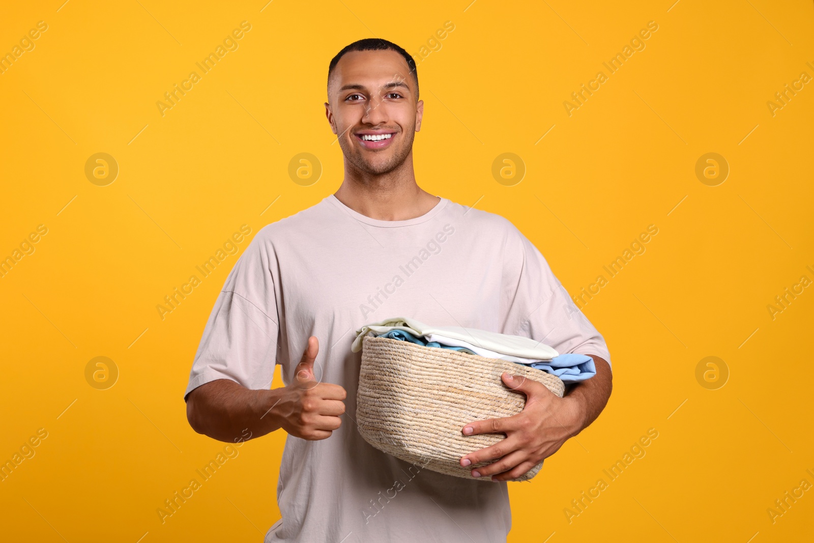 Photo of Happy man with basket full of laundry showing thumb up on orange background