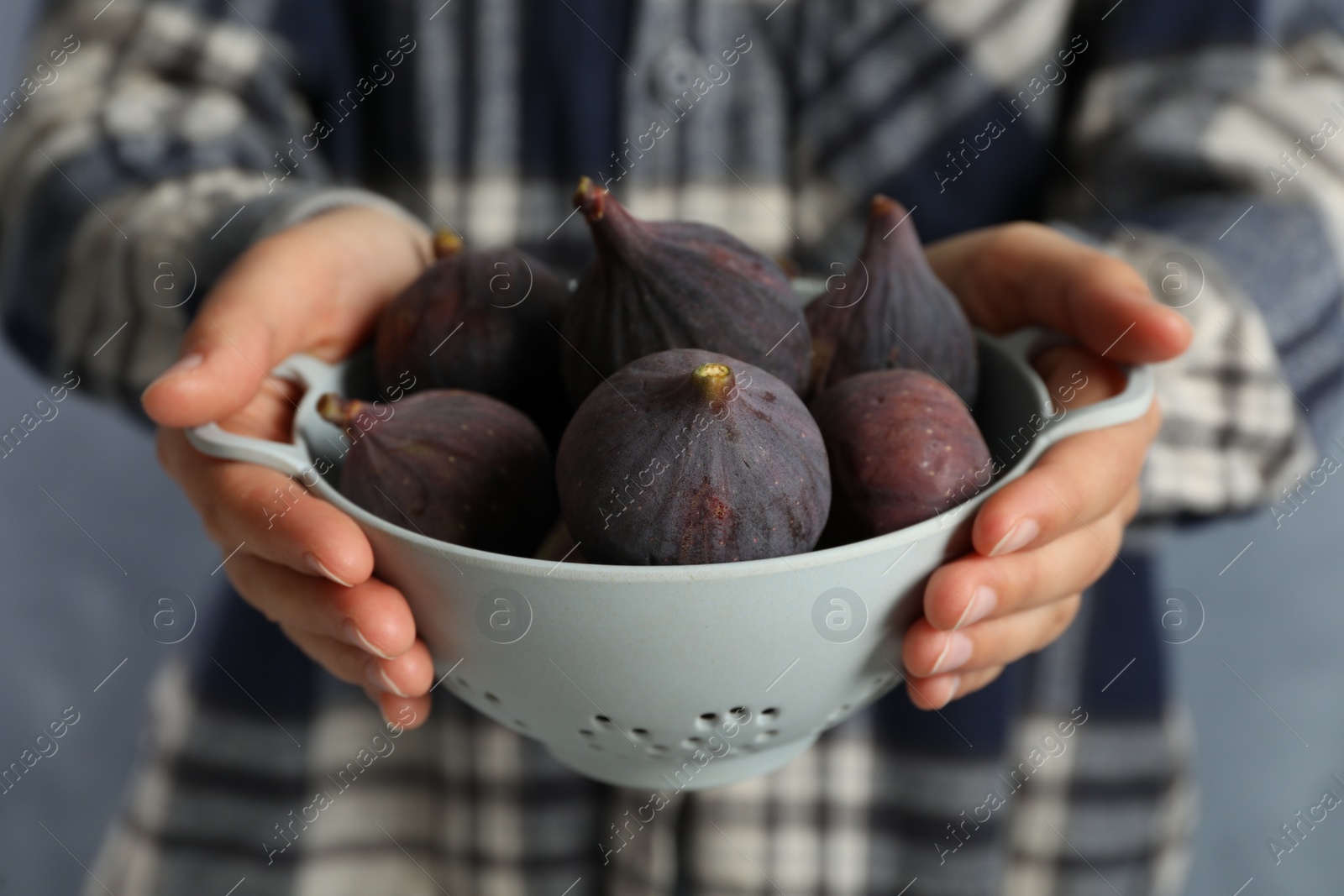 Photo of Woman holding colander with tasty raw figs on light blue background, closeup