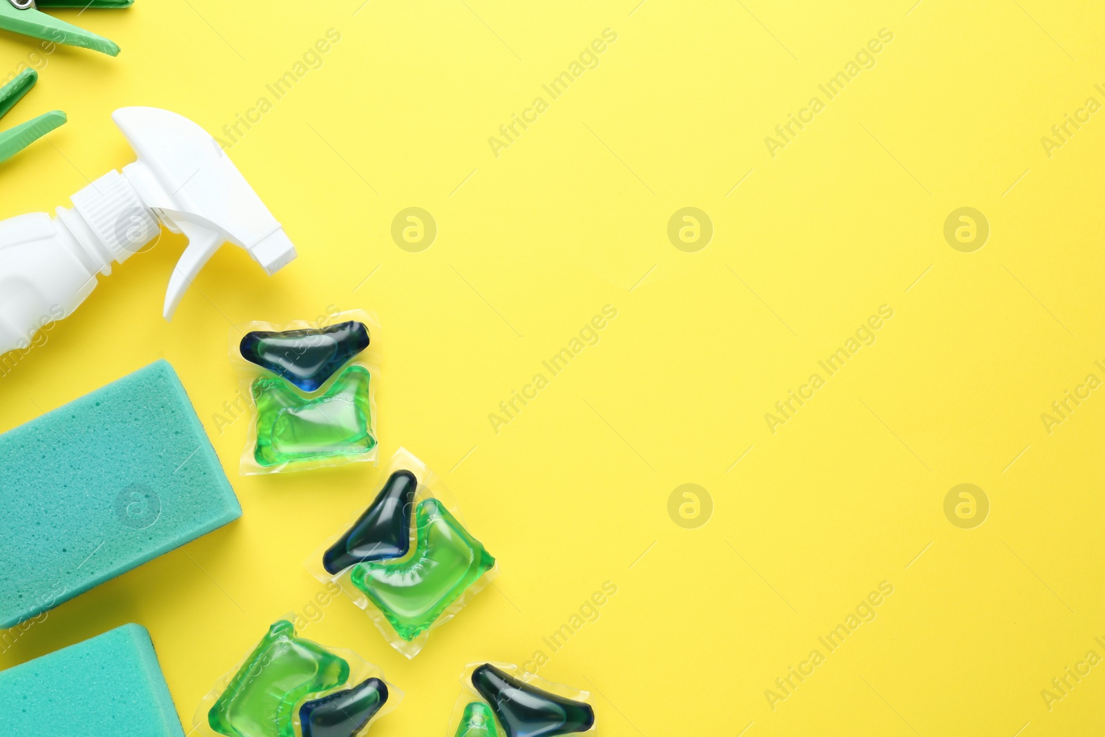 Photo of Laundry capsules, spray bottle and sponges on yellow background, flat lay. Space for text