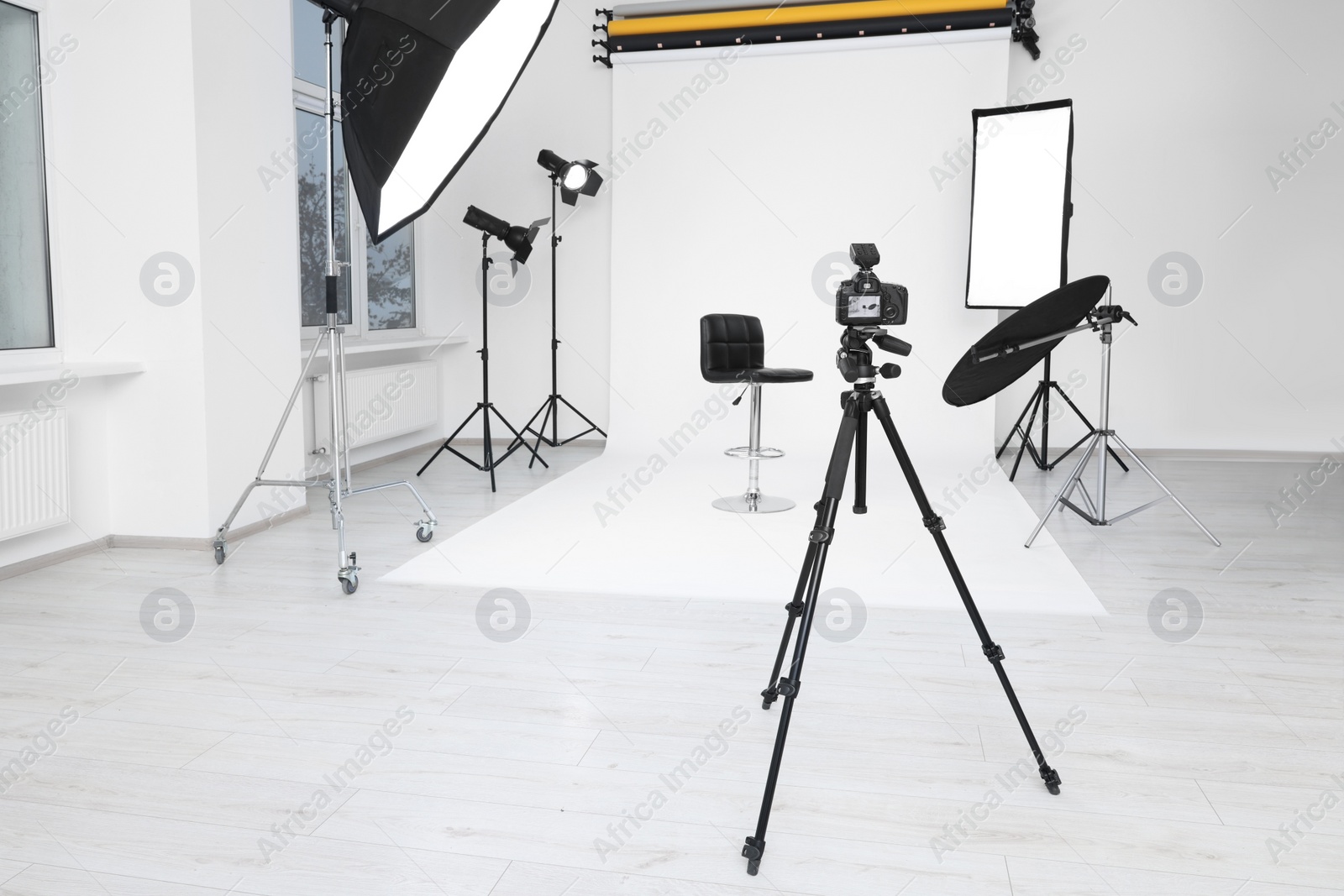 Photo of Camera on tripod, bar stool and professional lighting equipment in modern photo studio