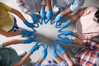 Photo of Group of people in blue medical gloves joining fingers indoors, top view