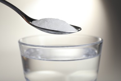 Photo of Spoon with baking soda over glass of water on light background, closeup