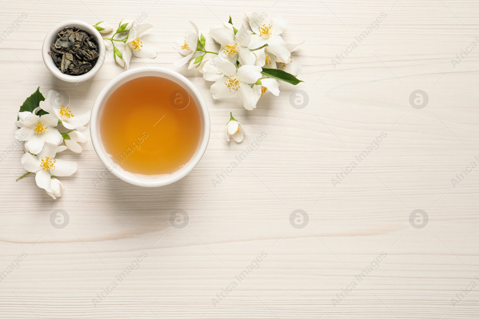 Photo of Aromatic jasmine tea, dry leaves and fresh flowers on white wooden table, flat lay. Space for text