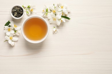 Photo of Aromatic jasmine tea, dry leaves and fresh flowers on white wooden table, flat lay. Space for text