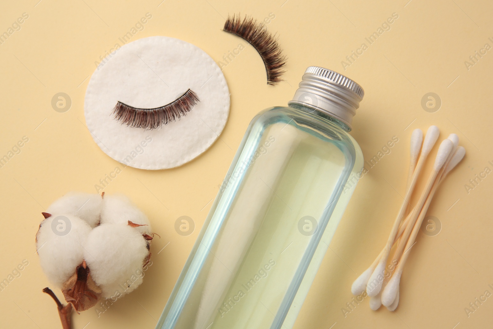 Photo of Bottle of makeup remover, cotton flower, pad, swabs and false eyelashes on yellow background, flat lay