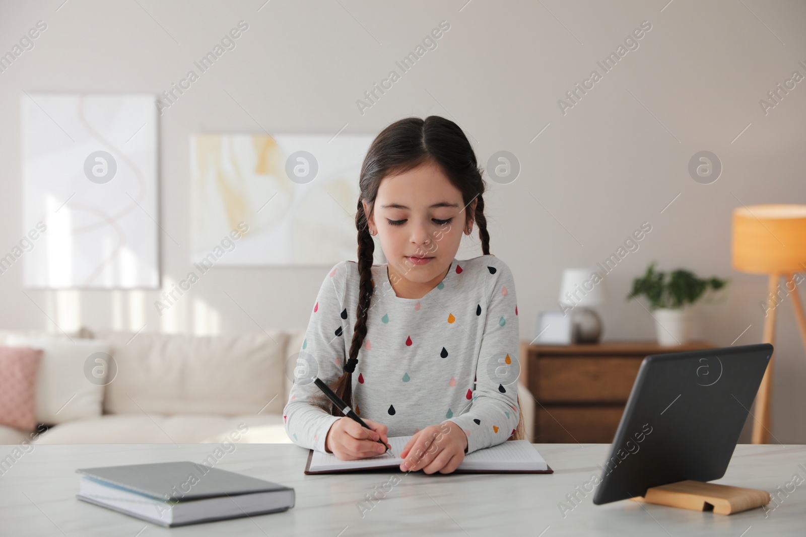 Photo of Little girl doing homework with modern tablet at home