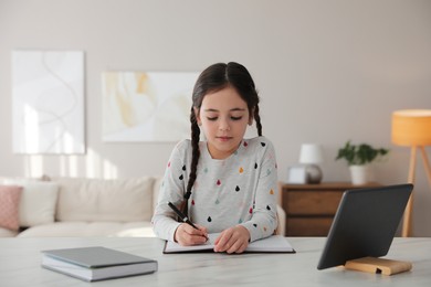 Photo of Little girl doing homework with modern tablet at home