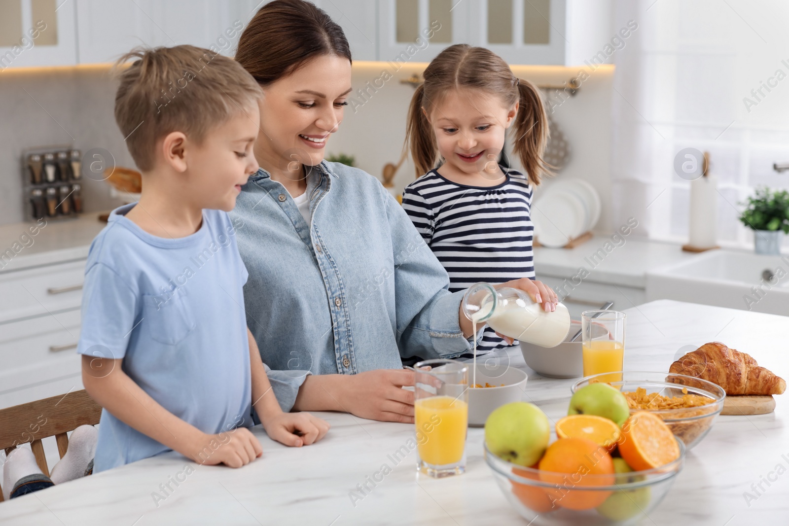 Photo of Mother and her little children having breakfast at table in kitchen