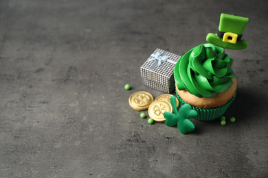 Decorated cupcake and gift box on grey table, space for text. St. Patrick's Day celebration