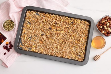 Photo of Making granola. Baking tray with mixture of oat flakes and other ingredients on white marble table, flat lay