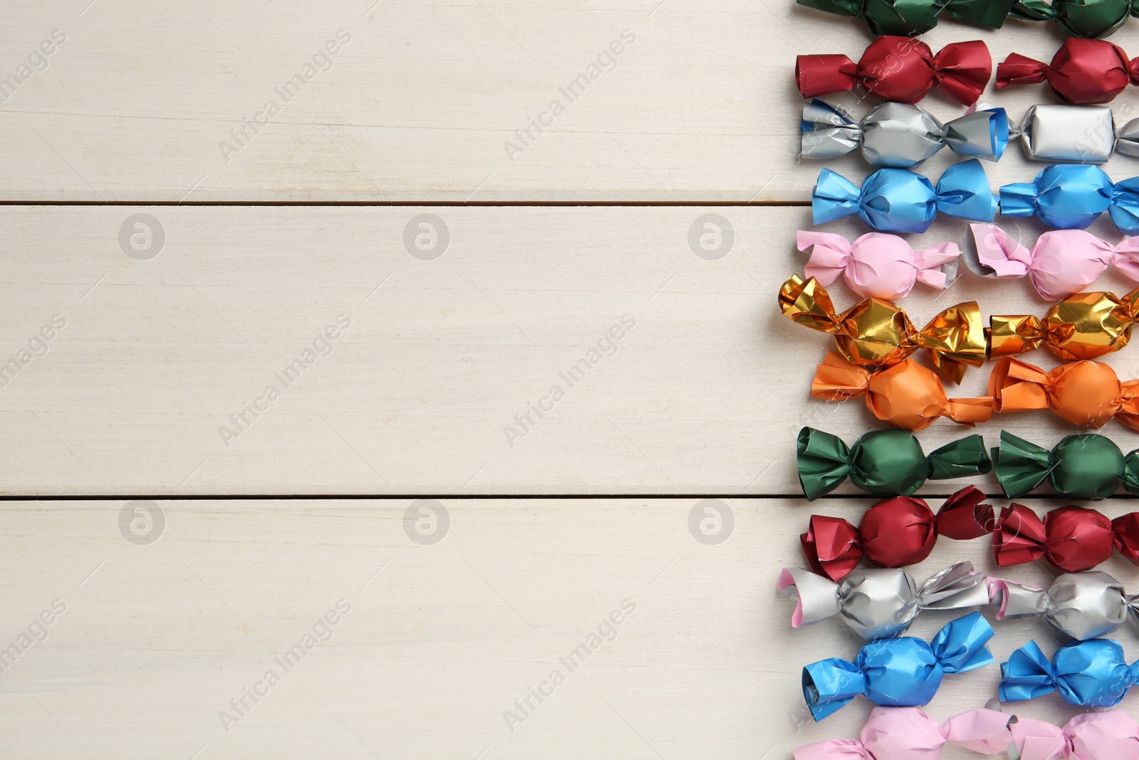 Photo of Candies in colorful wrappers on beige wooden table, flat lay. Space for text