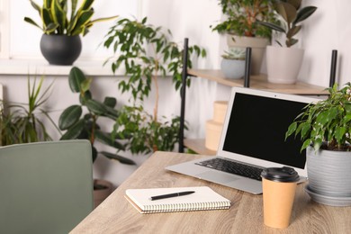 Photo of Paper cup, notebook and laptop on wooden table in room