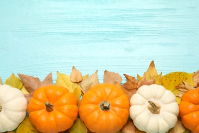 Flat lay composition with pumpkins and autumn leaves on light blue wooden table. Space for text