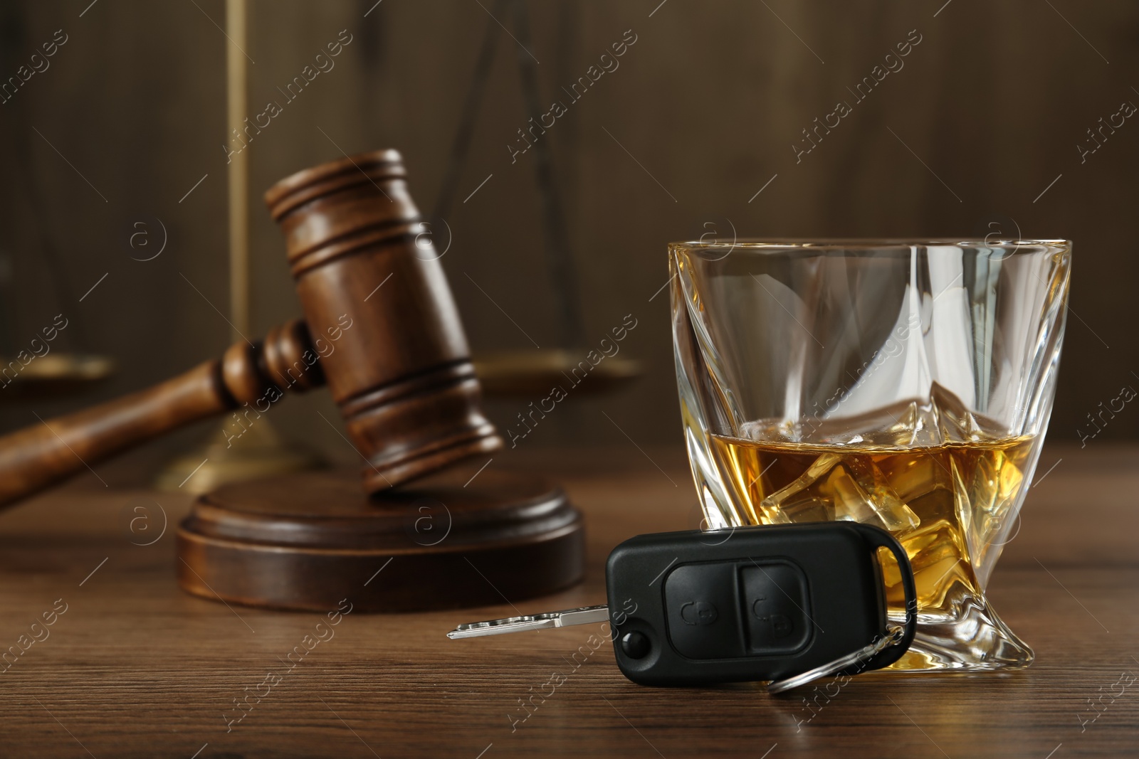 Photo of Car key, glass of alcohol near gavel on wooden table. Dangerous drinking and driving