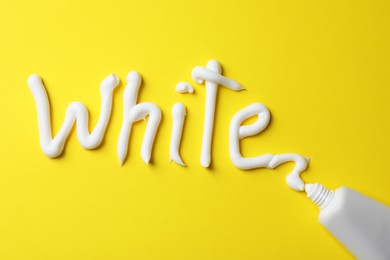 Photo of Word White written with toothpaste and tube on yellow background, top view