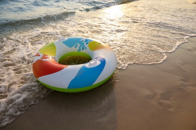 Bright inflatable ring on sunlit sandy beach near sea, space for text