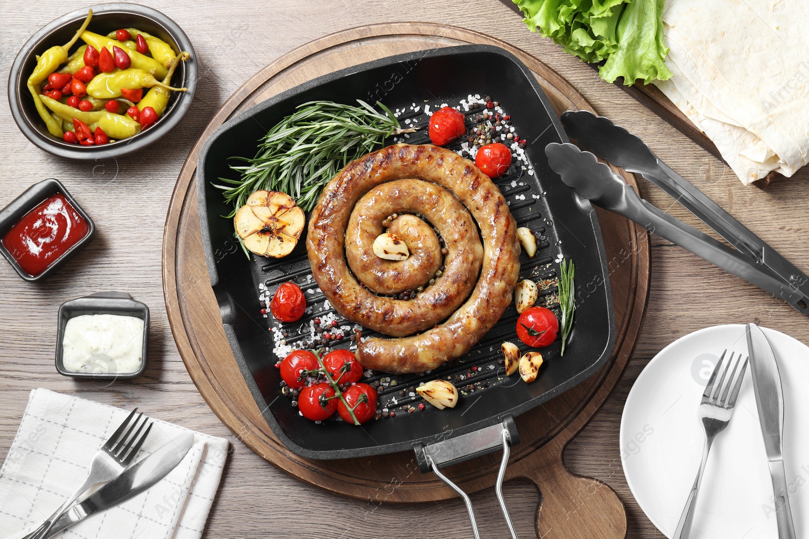 Photo of Delicious homemade sausage with garlic, tomatoes, rosemary and spices served on wooden table, flat lay