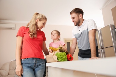 Happy young family with healthy food in paper bag at home