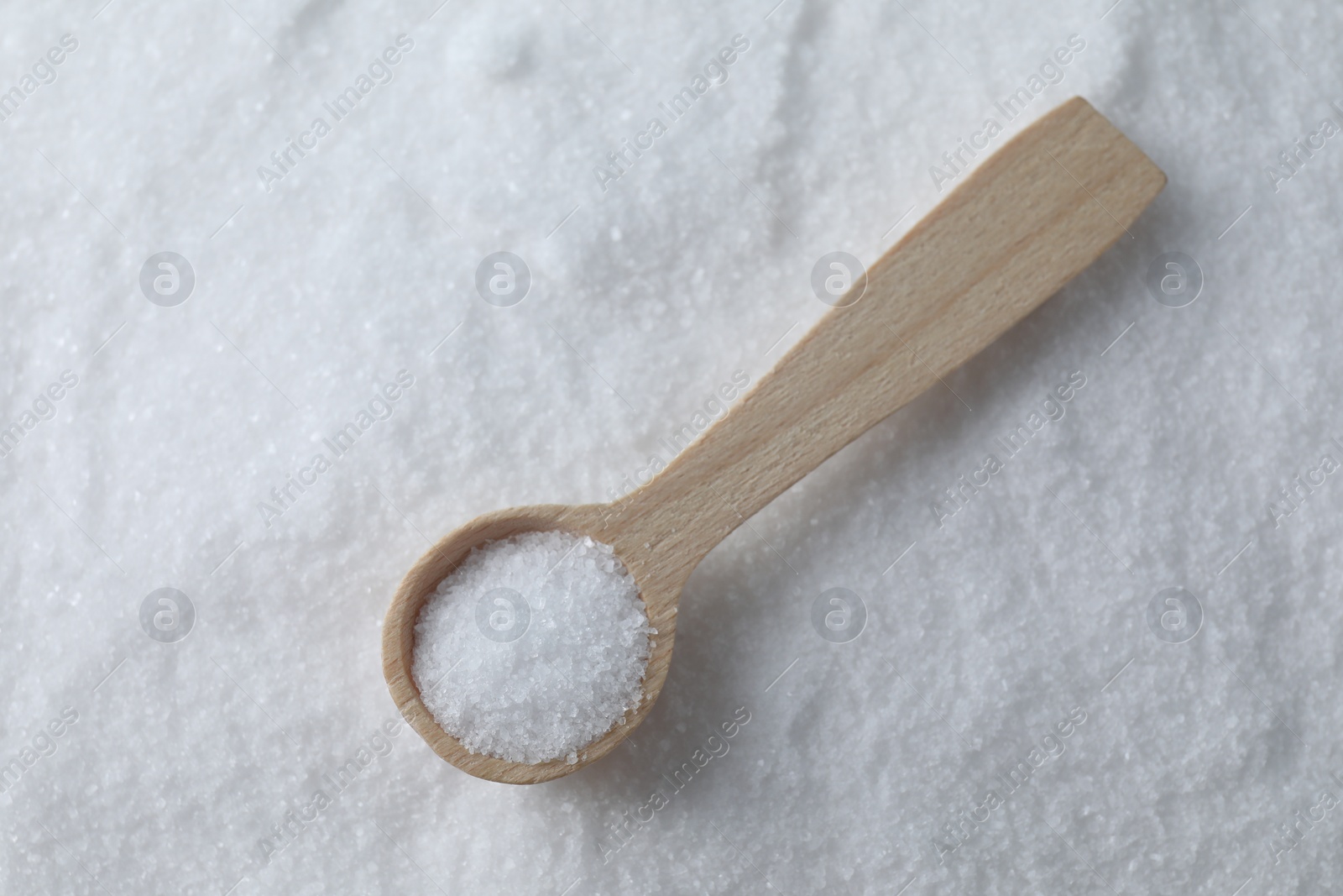 Photo of Wooden spoon on white sea salt, top view