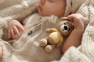 Photo of Adorable newborn baby with toy bear sleeping on knitted plaid