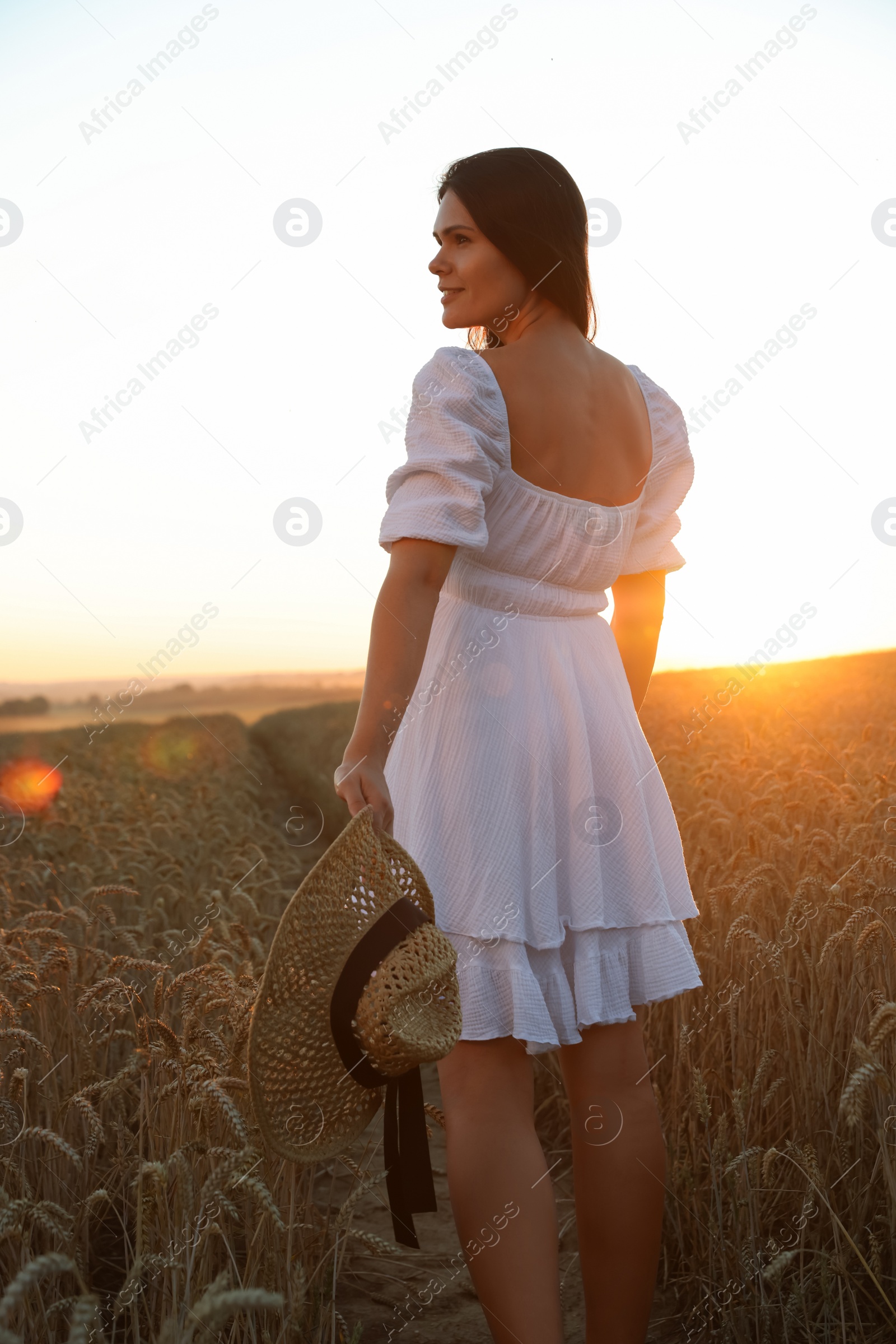 Photo of Beautiful young woman with straw hat in ripe wheat field at sunset