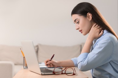 Photo of Young woman suffering from neck pain while working at table in office