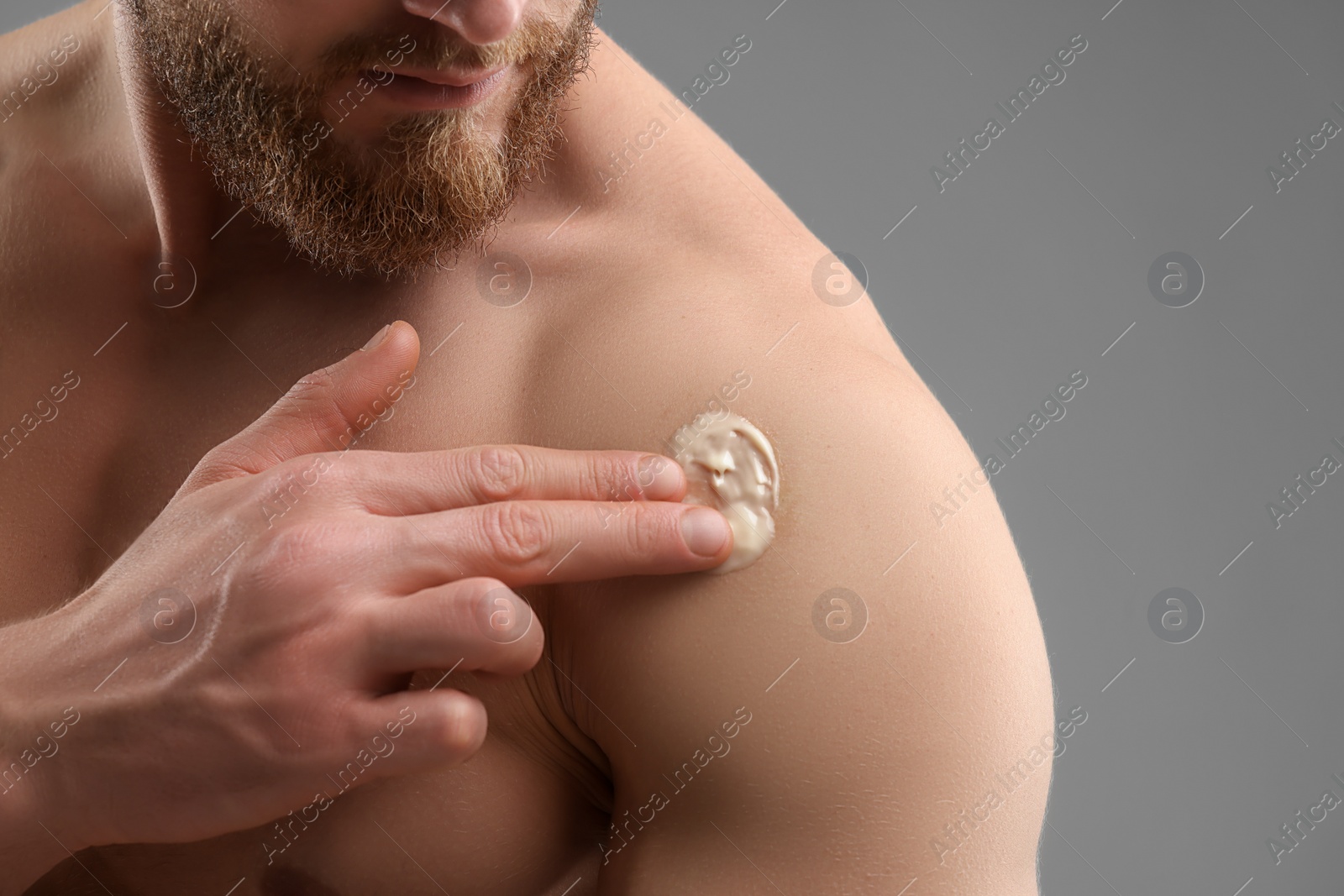 Photo of Man applying moisturizing cream onto his shoulder on grey background, closeup