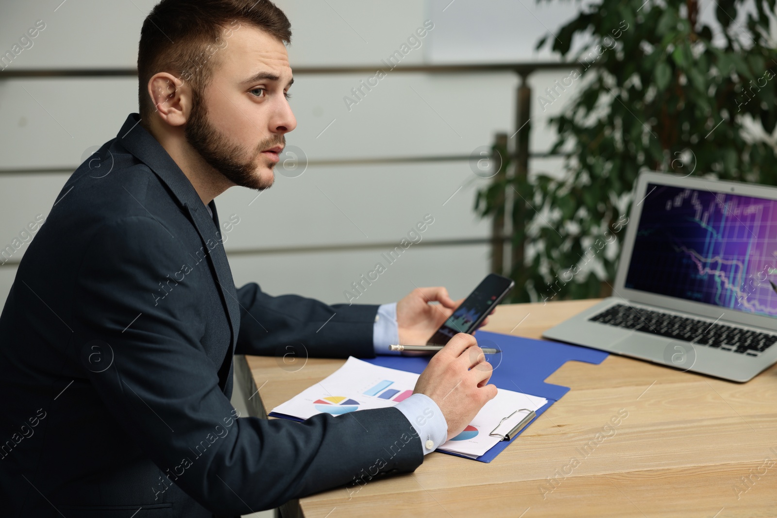 Photo of Forex trader working with smartphone and charts at table in office