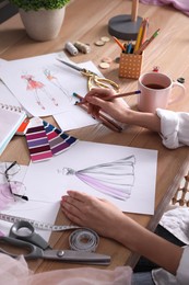 Photo of Fashion designer drawing sketch at wooden table, closeup