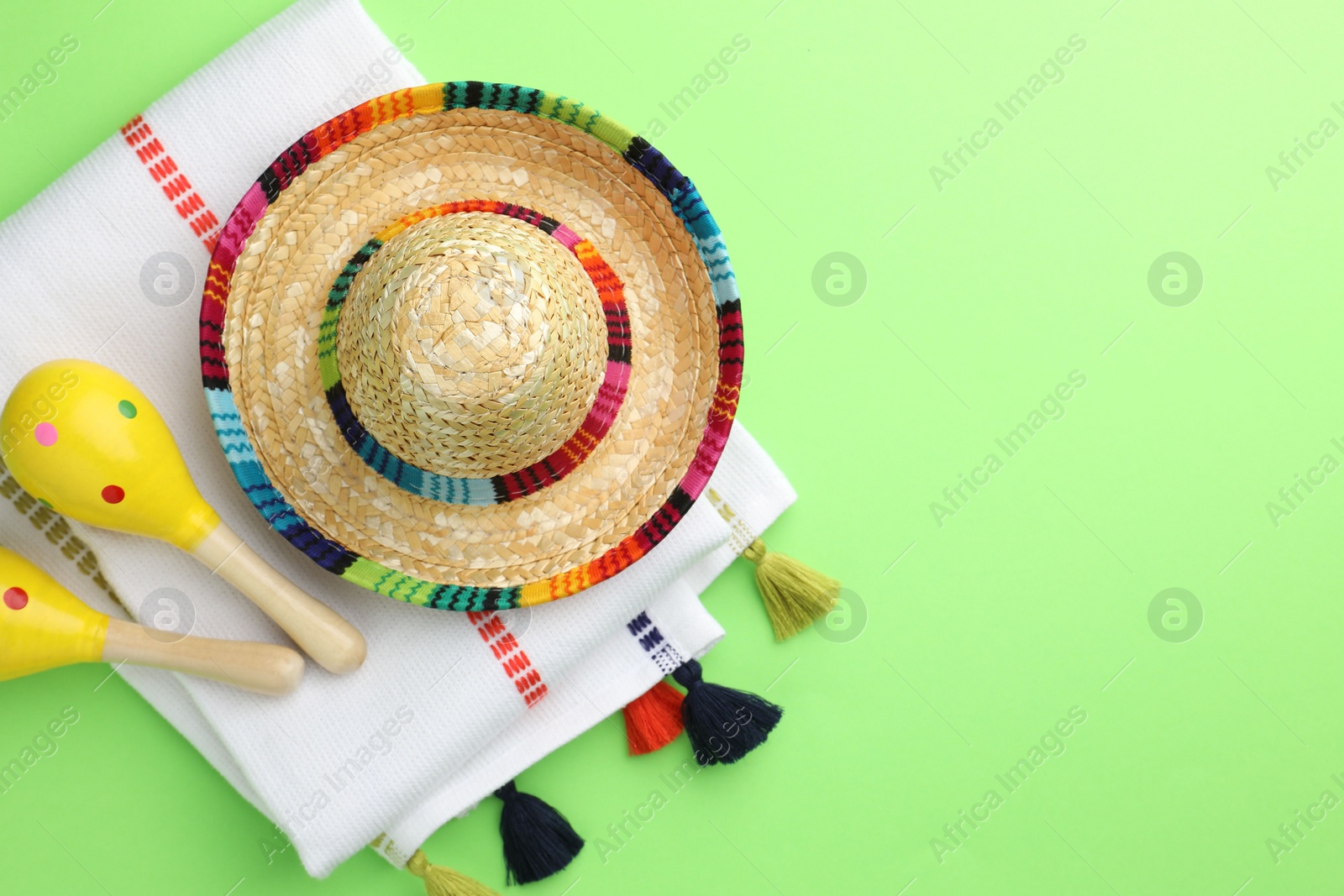 Photo of Mexican sombrero hat, maracas and poncho on green background, flat lay. Space for text
